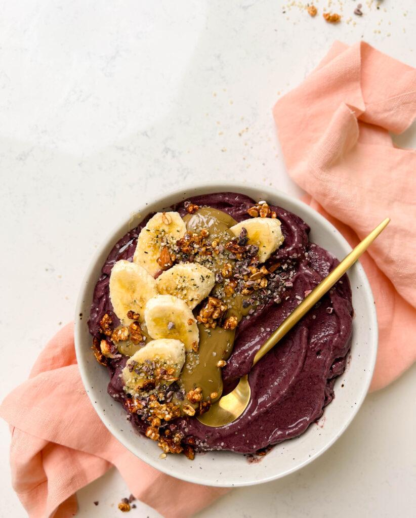 white bowl of acai with banana, granola and sunflower butter on top