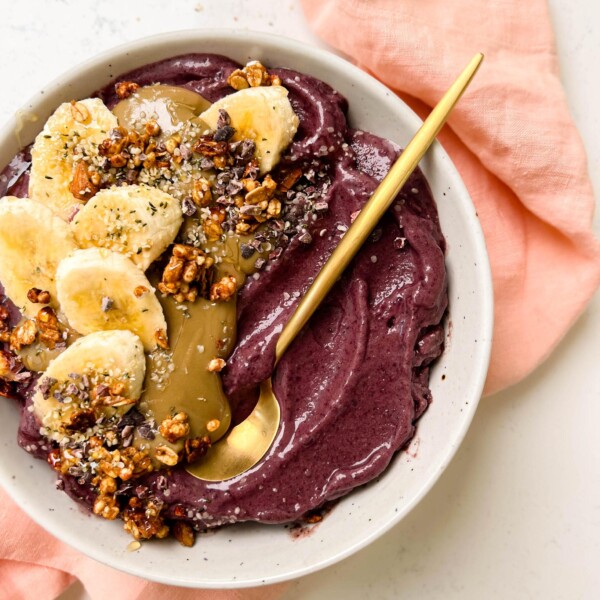 white bowl of acai with banana, granola and sunflower butter on top