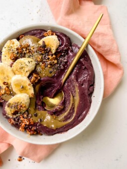 white bowl of acai with banana, granola and sunflower butter on top