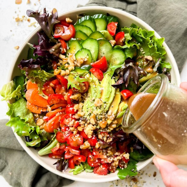 classic garden salad with tomatoes, carrots, avocado, greens and nuts in a bowl on a green linen cloth