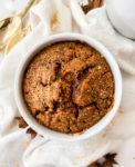 baked oats in a white ramekin next to a white cloth and cinnamon sticks