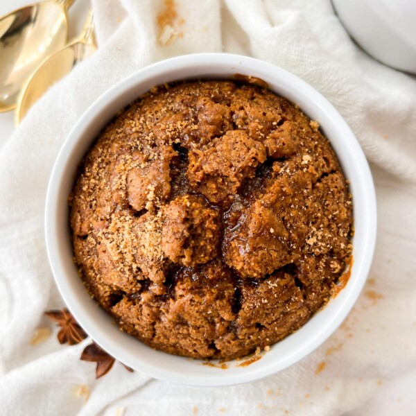 baked oats in a white ramekin next to a white cloth and cinnamon sticks