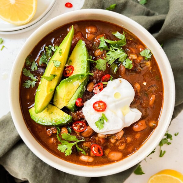 chili in a bowl with avocado, yogurt and spices on top next to a green cloth and lemons