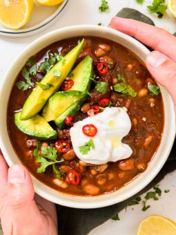 chili in a bowl with avocado, yogurt and spices on top next to a green cloth and lemons