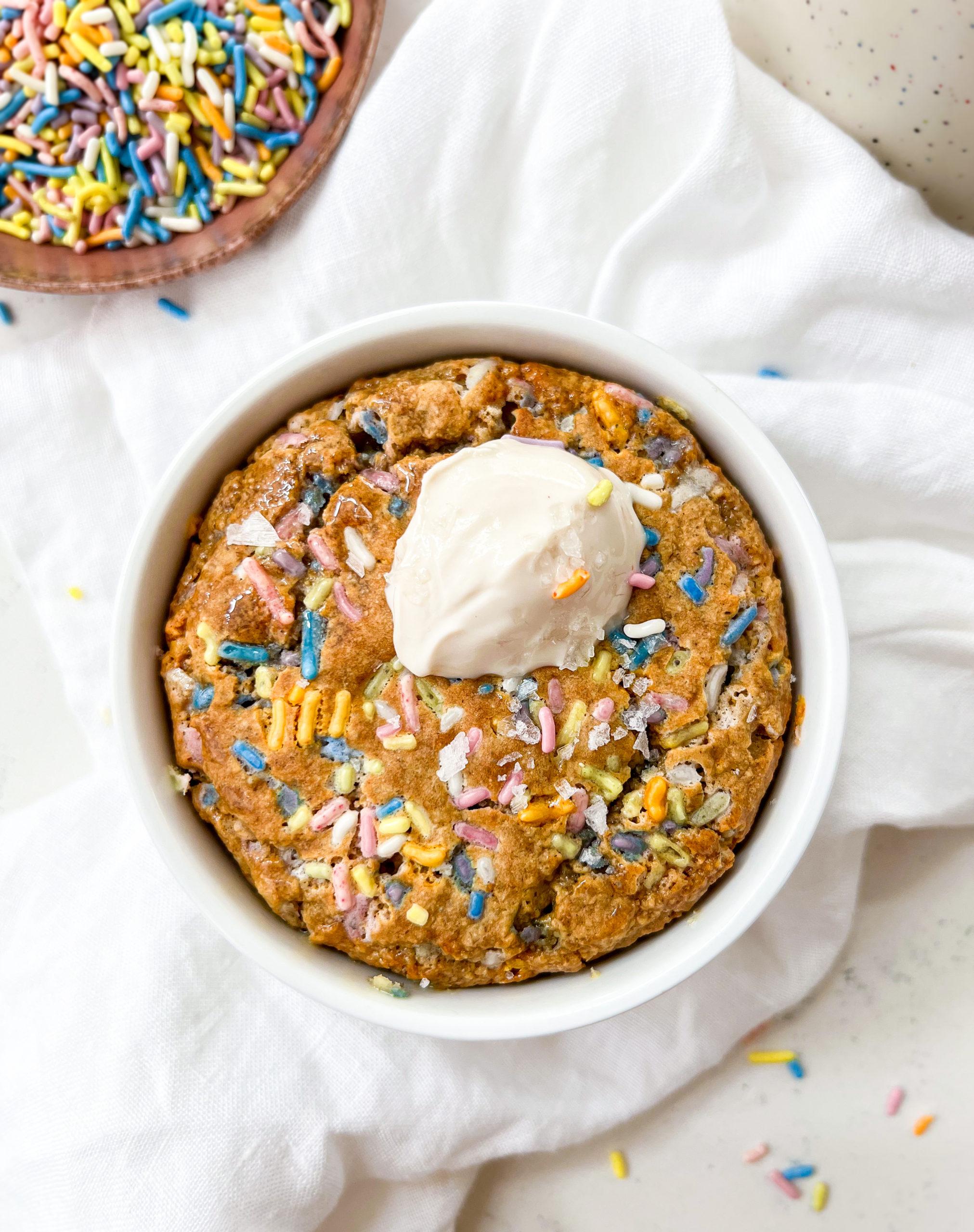 baked oats in a ramekin next to a bowl of sprinkles