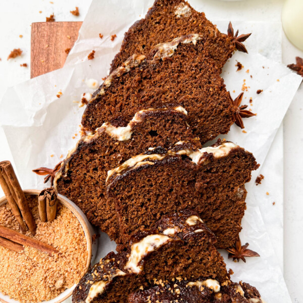 vegan gingerbread loaf slices on parchment paper next to a bowl of coconut sugar and white plates