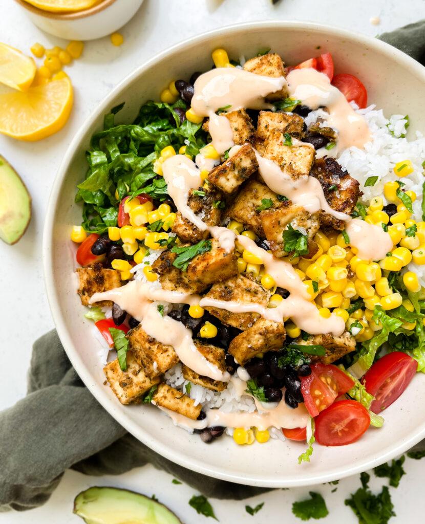 vegan chipotle burrito bowl on a green linen cloth next to lemon wedges and avocado