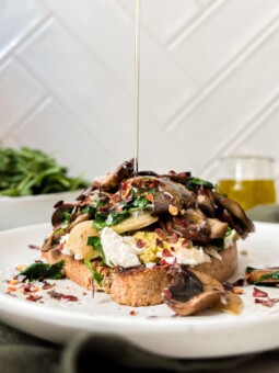 toast with mushrooms and ricotta on a white plate with oil poured on top