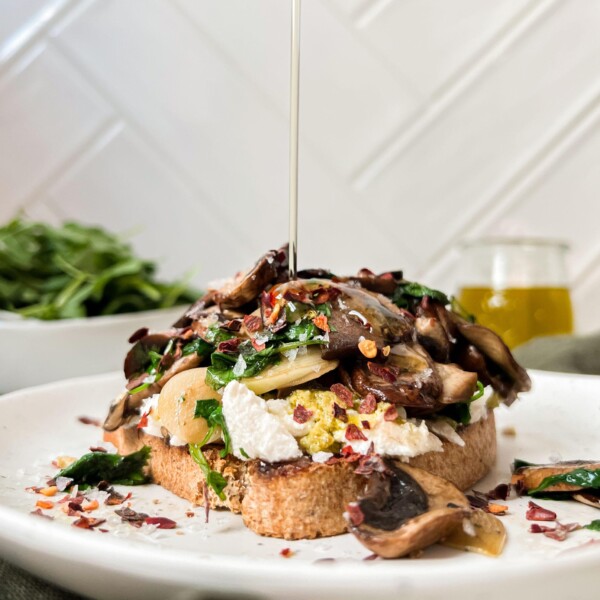 toast with mushrooms and ricotta on a white plate with oil poured on top