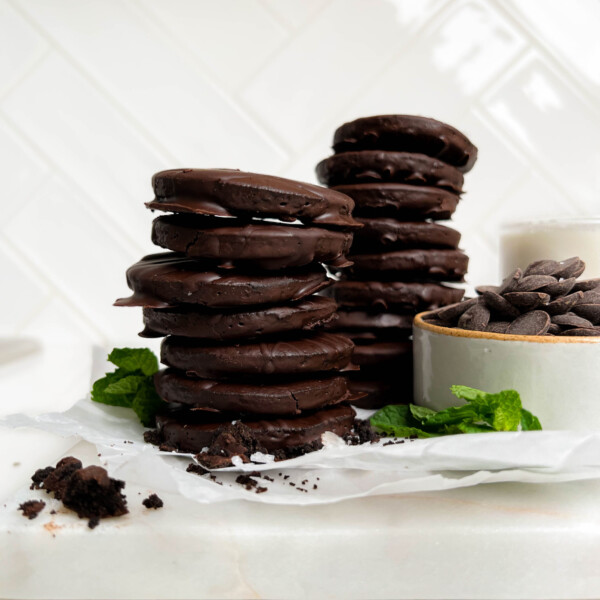 vegan thin mints on a cutting board with mint leaves and a bowl of chocolate chips