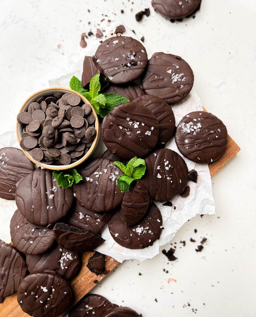 vegan thin mints on a cutting board with mint leaves and a bowl of chocolate chips