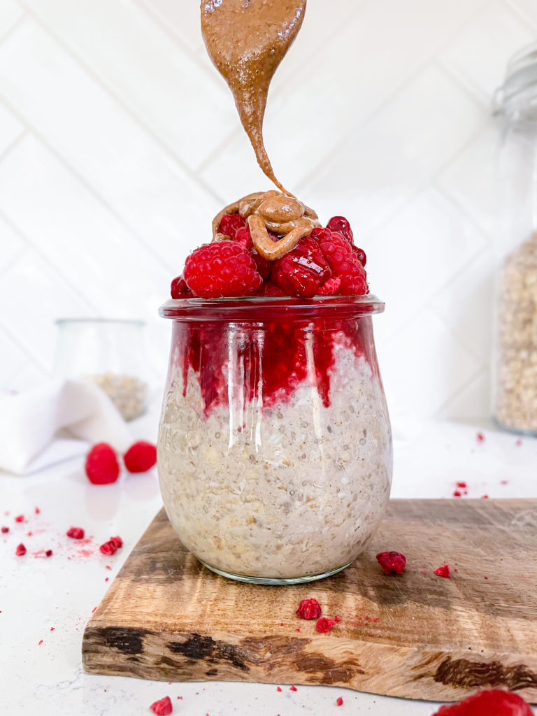 overnight oats, topped with raspberry jam, fresh raspberries and peanut butter in a glass jar.