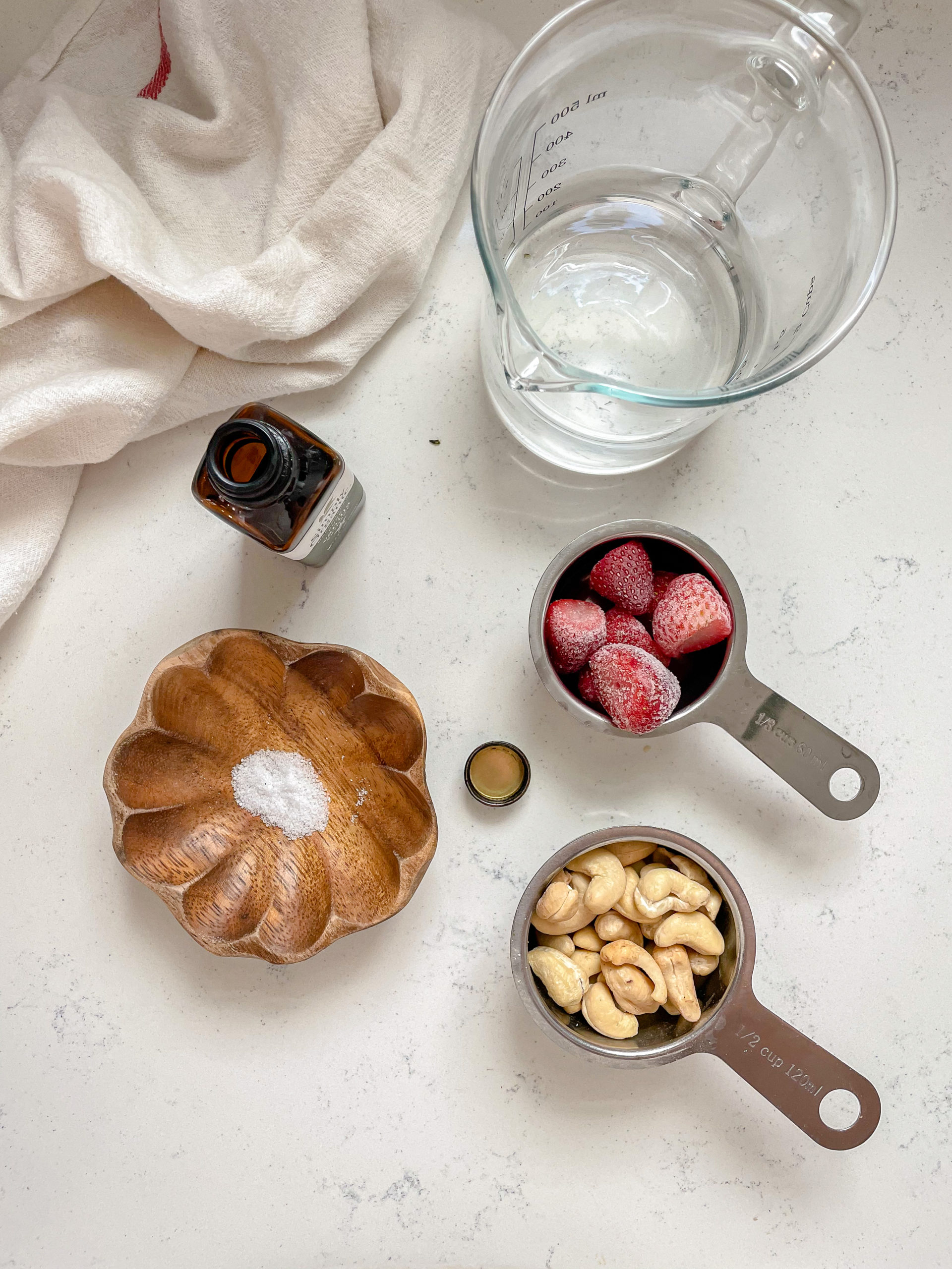 an array of ingredients for strawberry milk, cashews, salt, vanilla extract and strawberries. 