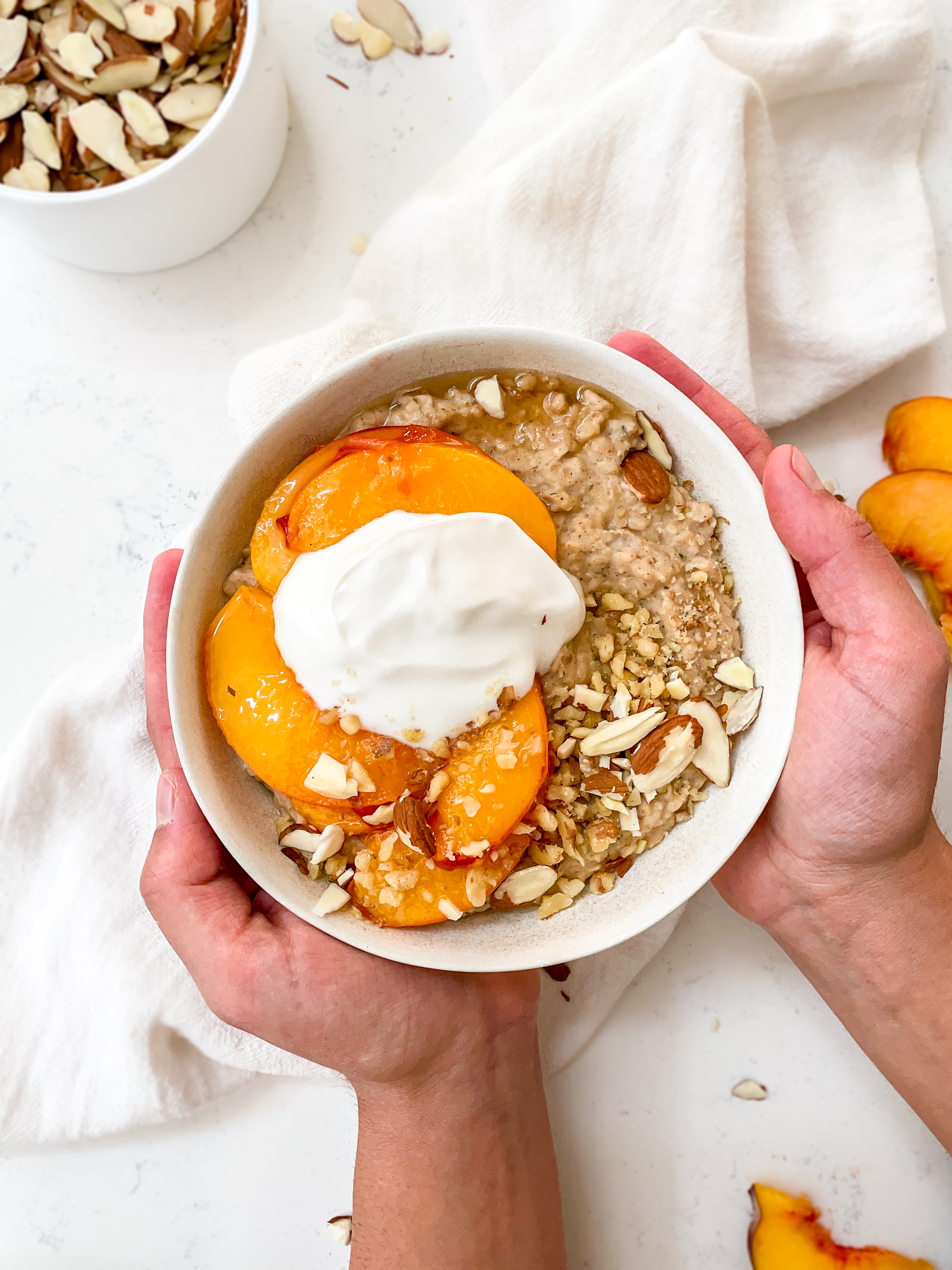 almond oatmeal with peaches on top and coconut yogurt dolloped on top with flaked almonds 