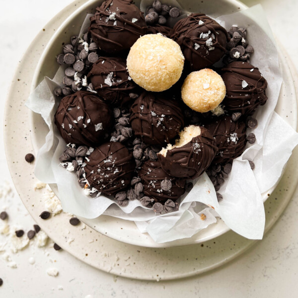 bounty balls in a white bowl next to a glass of milk and a bowl of shredded coconut