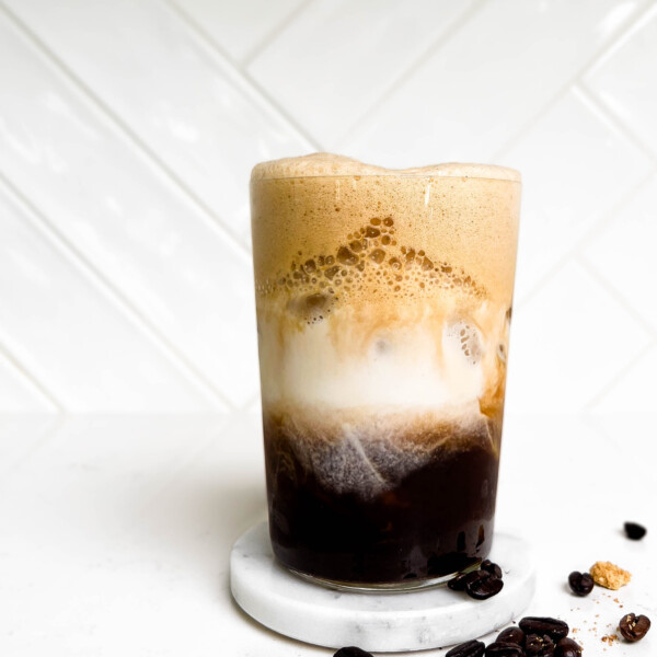 glass of iced espresso with milk with coffee beans spilled on the counter