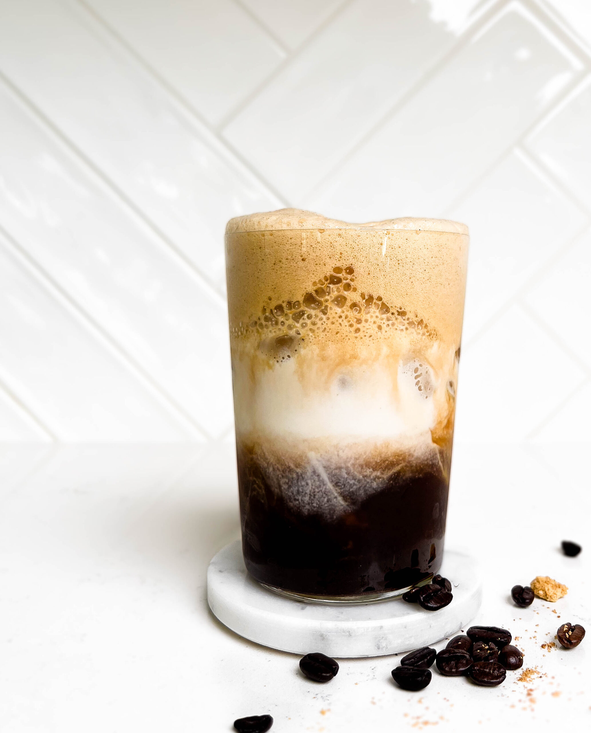 glass of iced espresso with milk with coffee beans spilled on the counter