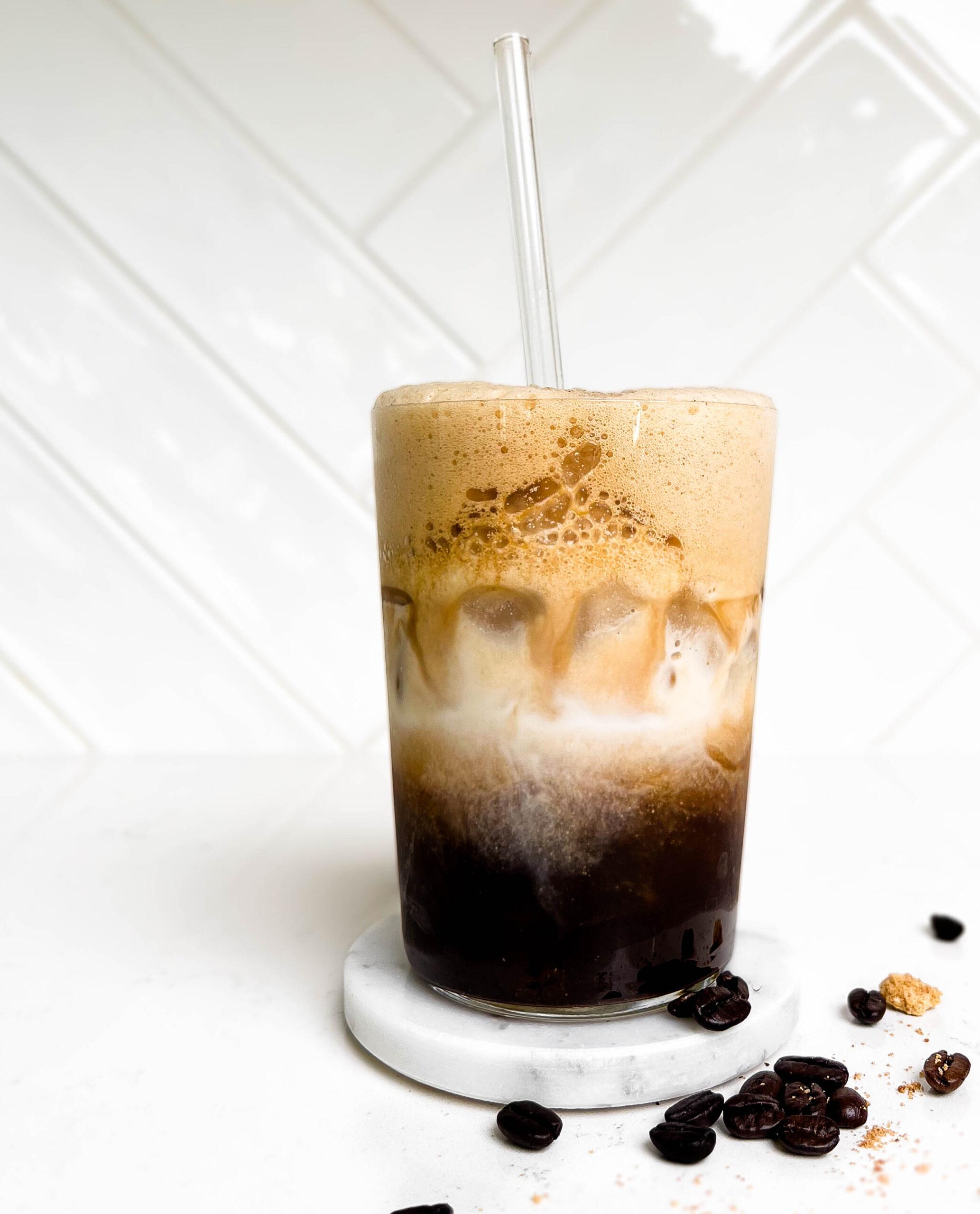 glass of iced espresso with milk with coffee beans spilled on the counter