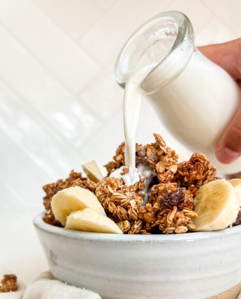 cinnamon and honey granola in white bowl with milk poured on top