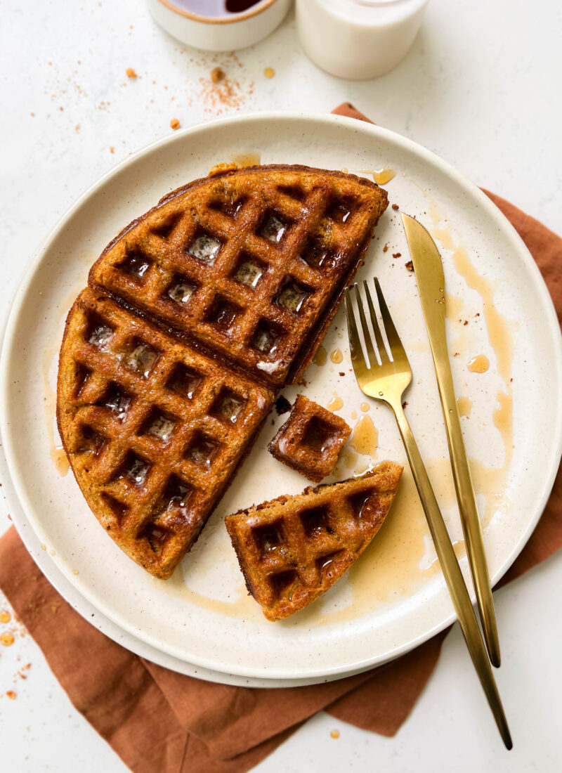 pumpkin waffle on a beige plate with gold flatware
