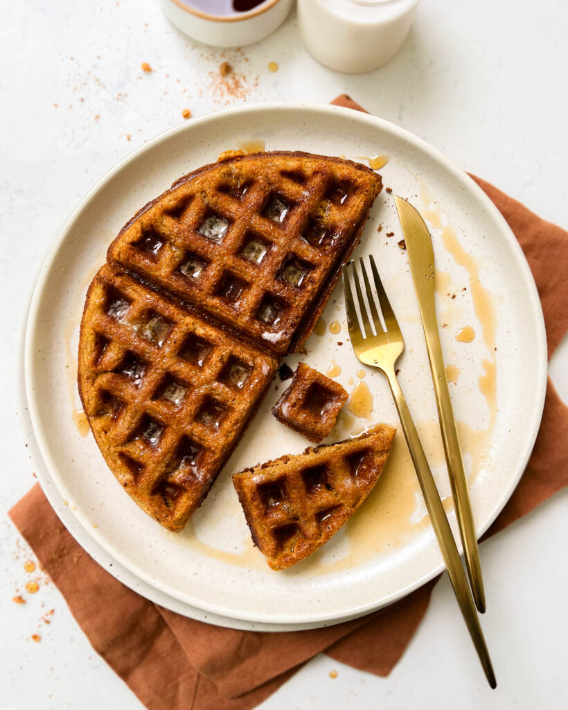 pumpkin waffle on a beige plate with gold flatware