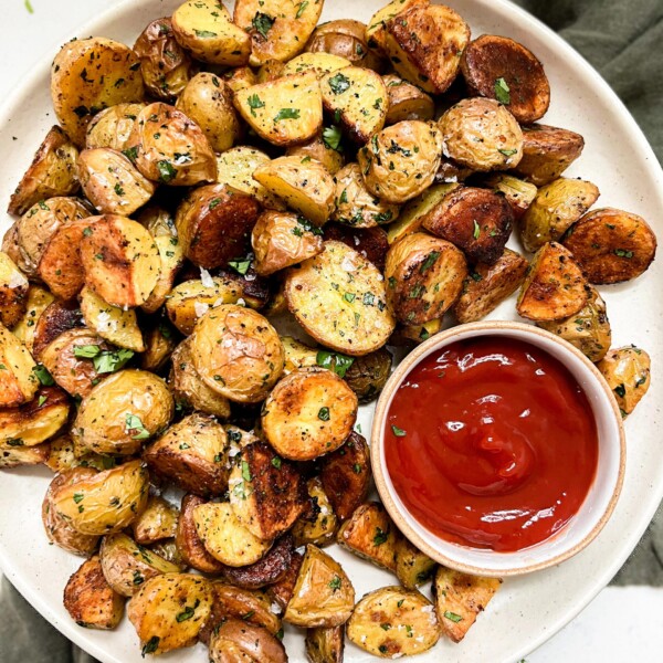 crispy oven baked potatoes on a beige plate next to a bowl of ketchup