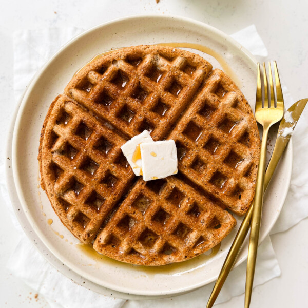 vegan waffle on a beige plate next to a glass of milk