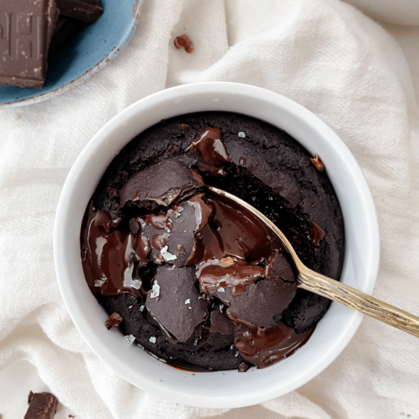 brownie in a mug next to a bowl of chocolate