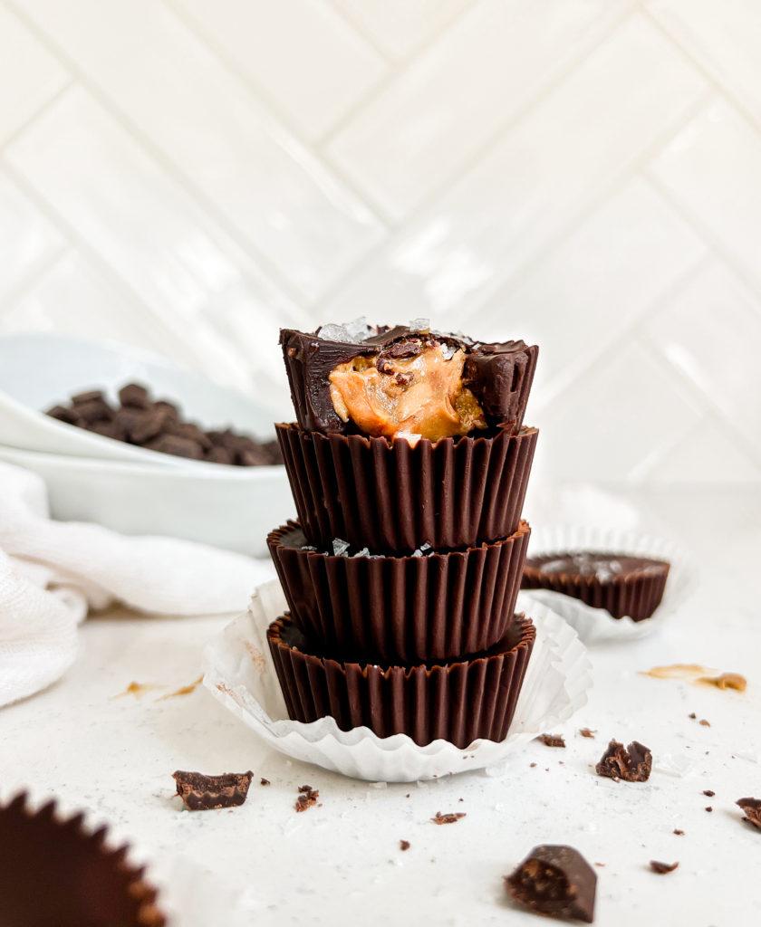sunflower butter cups stacked on one another next to broken pieces of chocolate