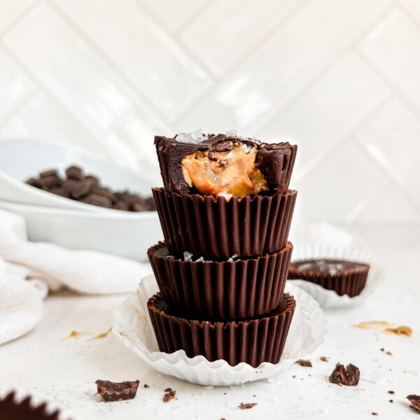 sunflower butter cups stacked on one another next to broken pieces of chocolate