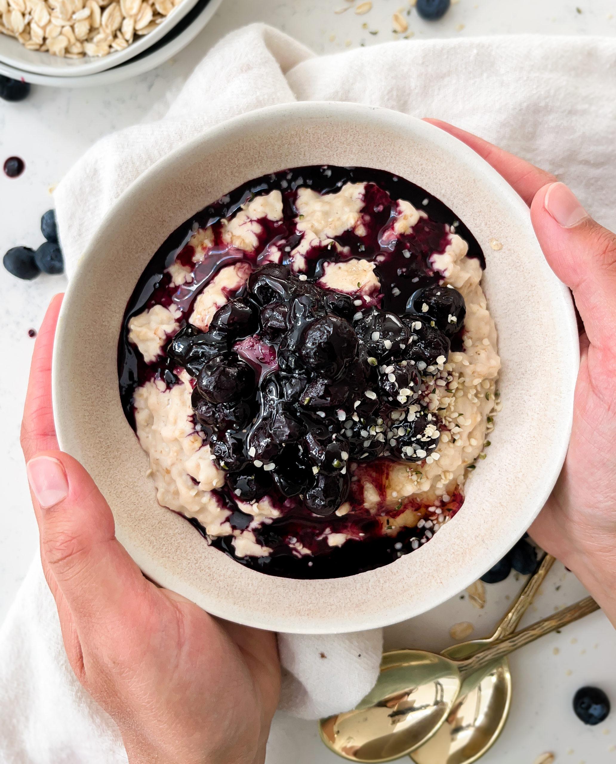 oatmeal in a bowl with blueberries on top next to gold spoons and a bowl of rolled oats