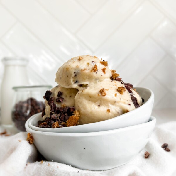 smoothie in a white bowl next to a jar of milk and cacao nibs