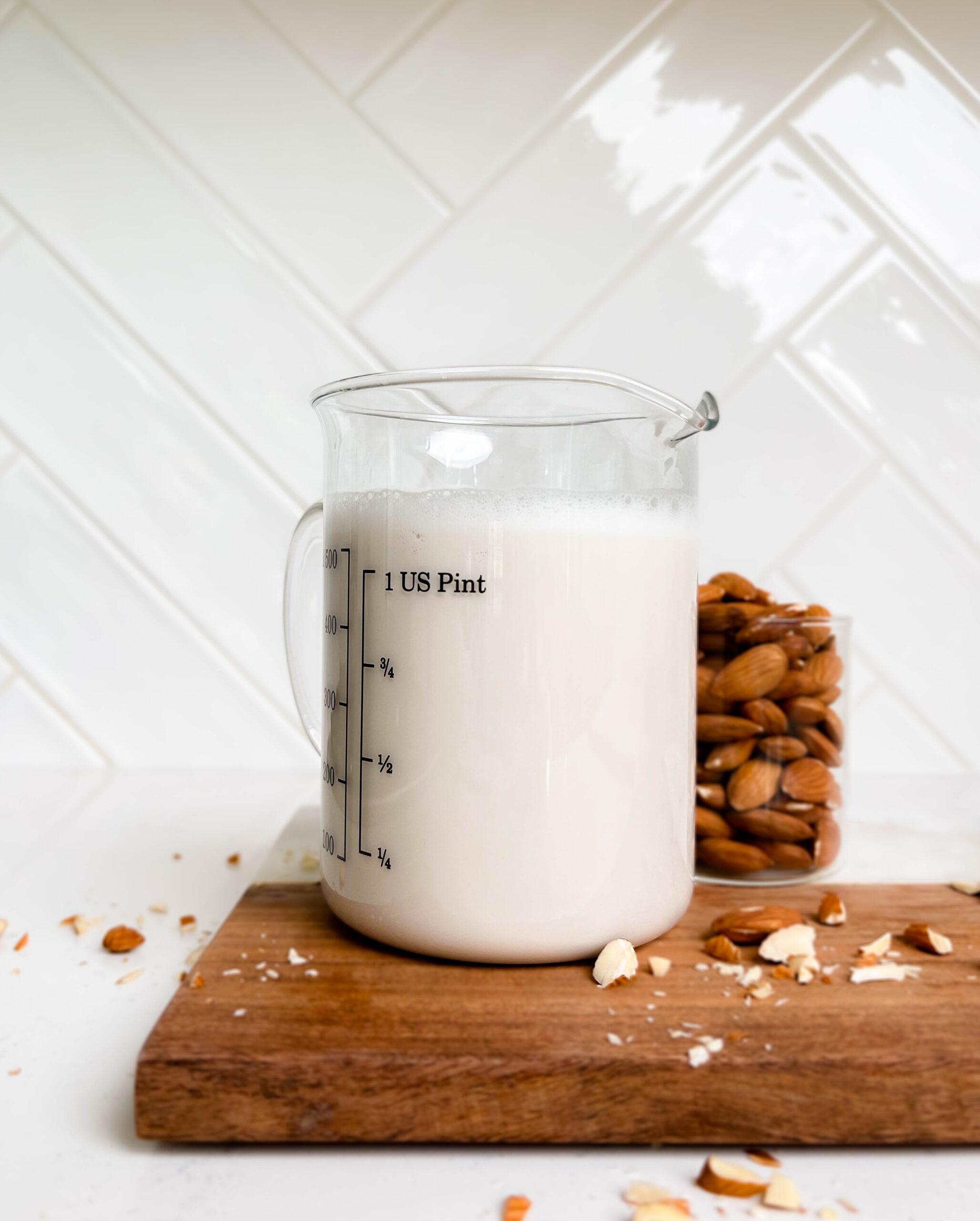 homemade almond milk in a glass pitcher on a wooden cutting board