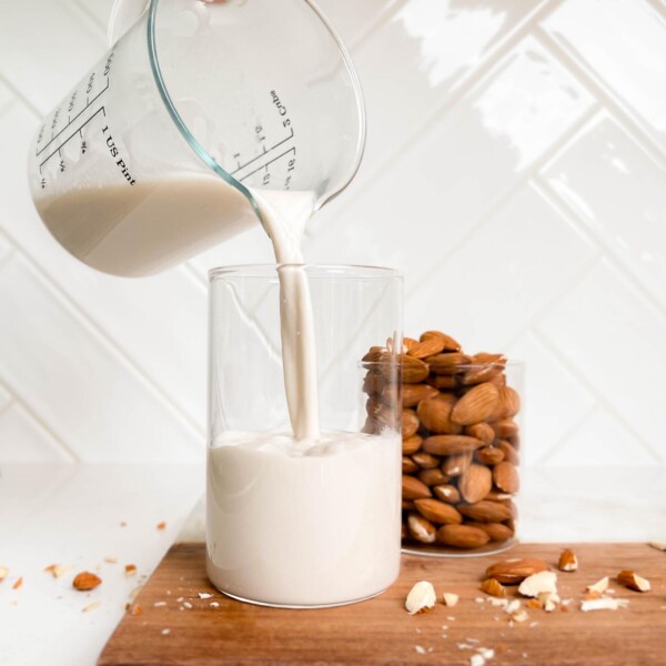 almond milk pouring into a glass cup on a cutting board