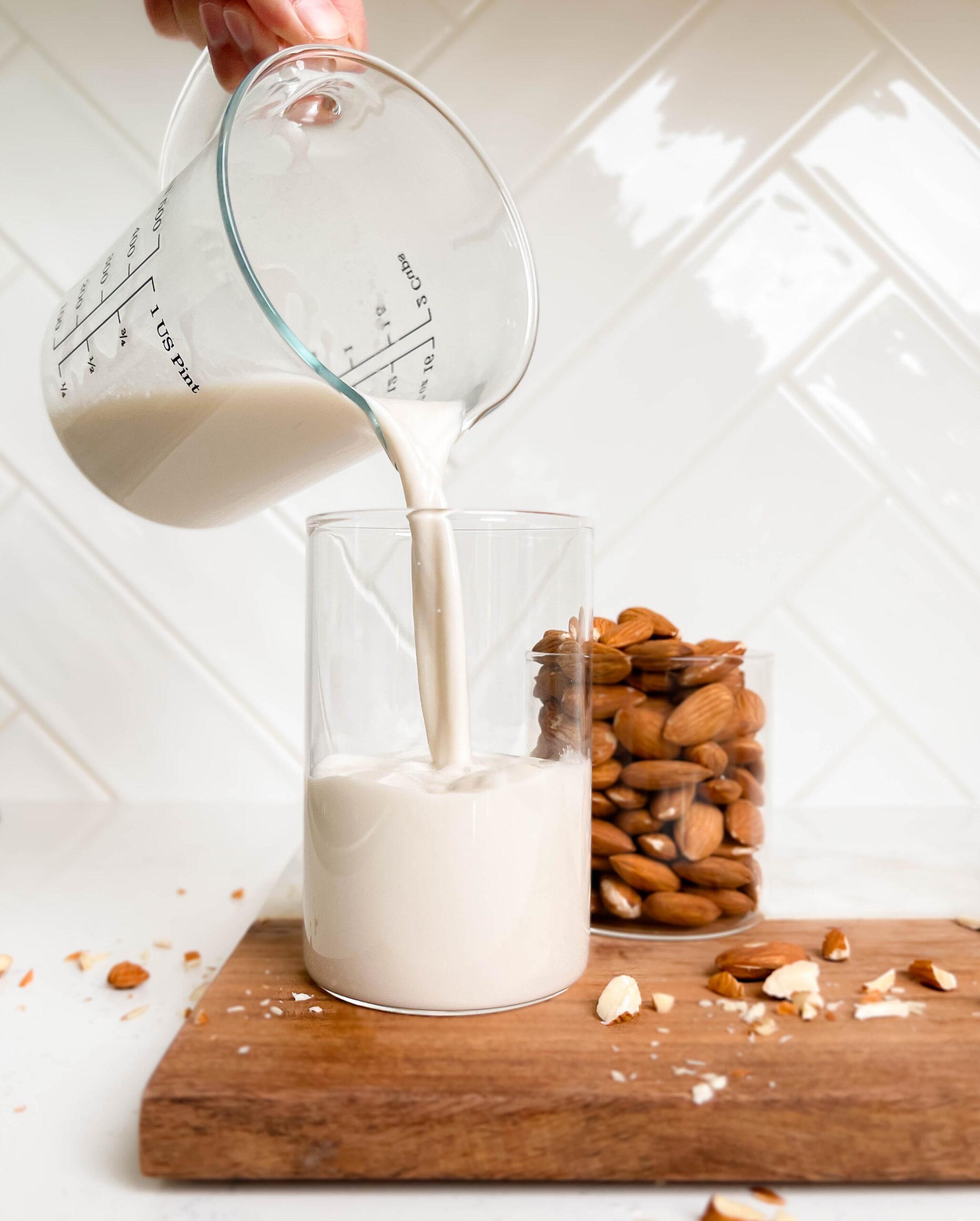 almond milk pouring into a glass cup on a cutting board