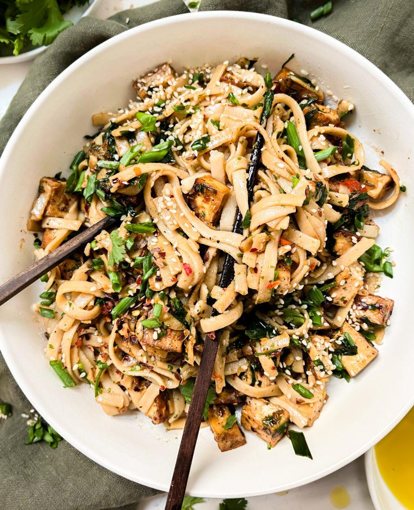 chili oil noodles in a white bowl with chopsticks next to a green napkin