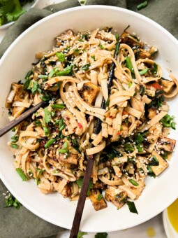 chili oil noodles in a white bowl with chopsticks next to a green napkin