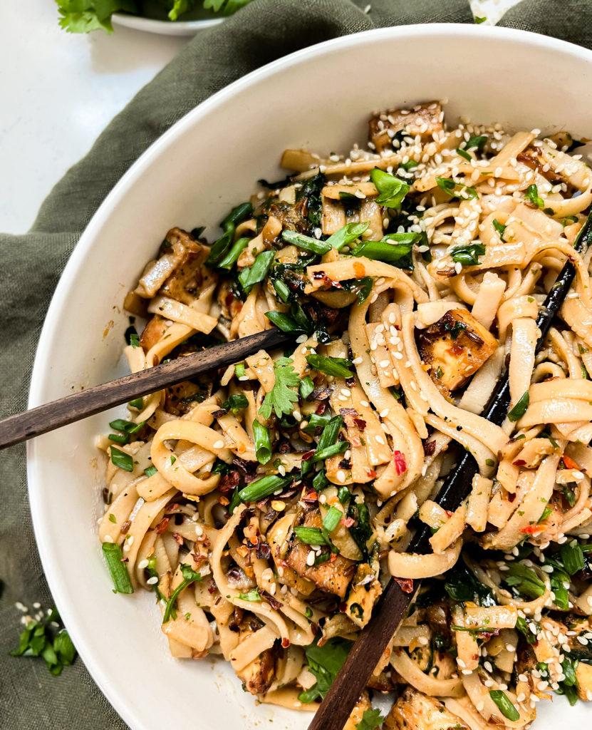 garlic chili oil noodles in a white bowl with chopsticks next to a green napkin