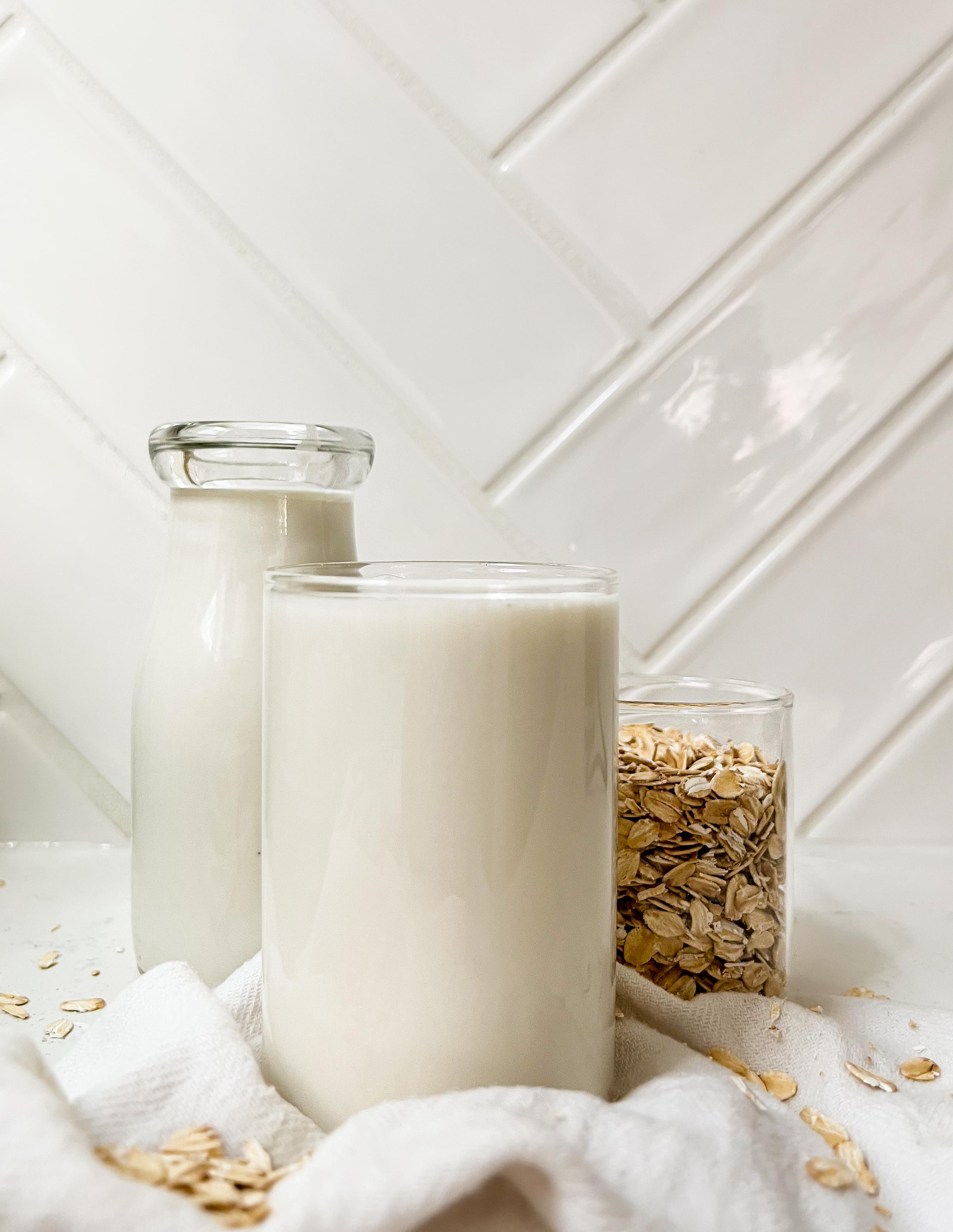 oat milk in a cup next to a jar of milk and oats