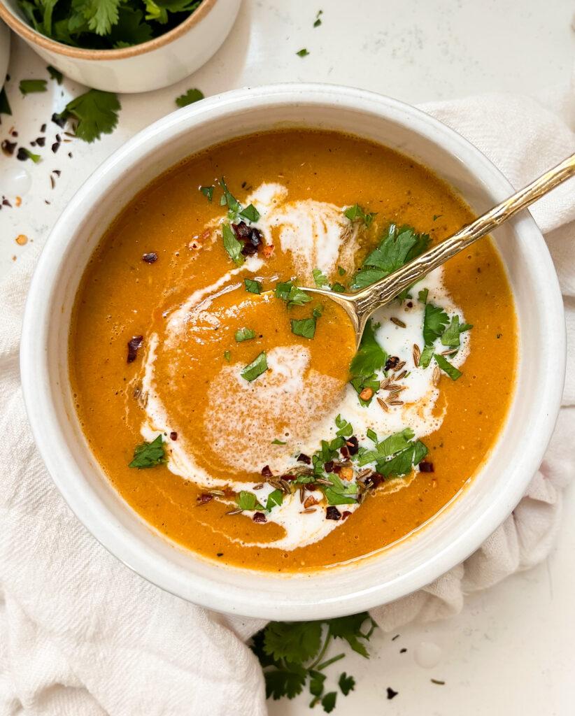 creamy red lentil soup in a white bowl next to a bowl of cilantro