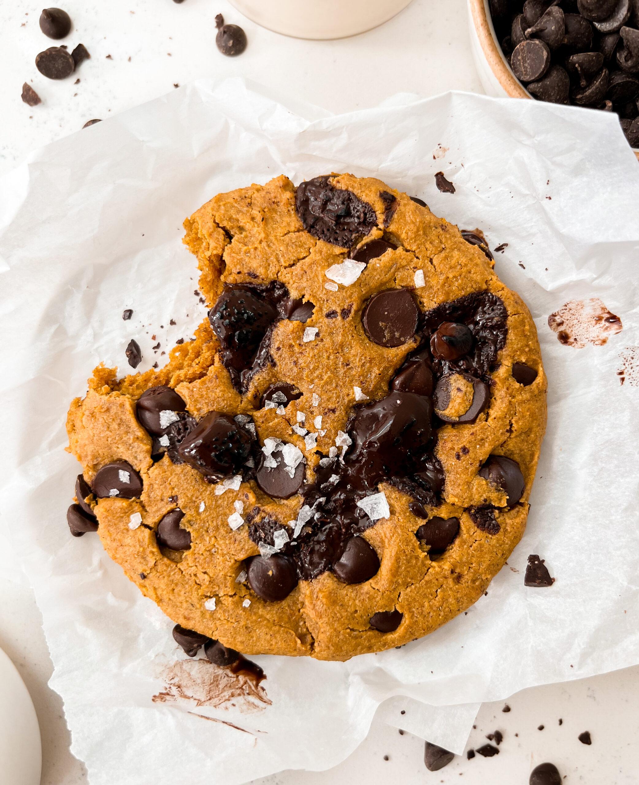 single-serve pumpkin chocolate chip cookie on parchment paper next to a bowl of chocolate chips