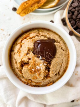 vegan banana bread baked oats in a white ramekin next to a banana peel and chocolate chips