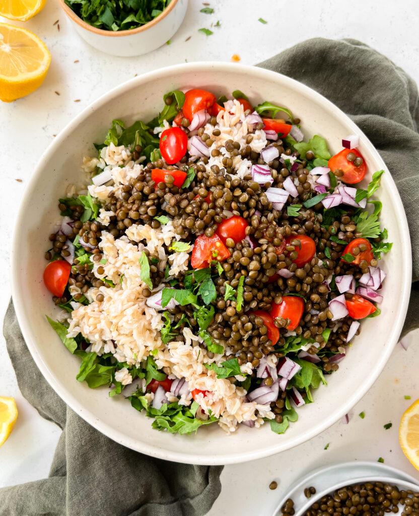 spicy vegan lentil salad with tahini dressing in a beige bowl on a green linen napkin next to lemons
