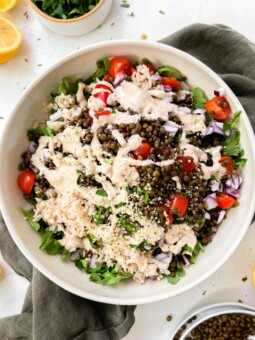 spicy vegan lentil salad with tahini dressing in a beige bowl on a green linen napkin next to lemons