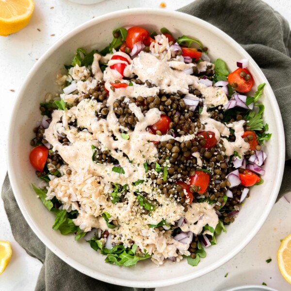 spicy vegan lentil salad with tahini dressing in a beige bowl on a green linen napkin next to lemons