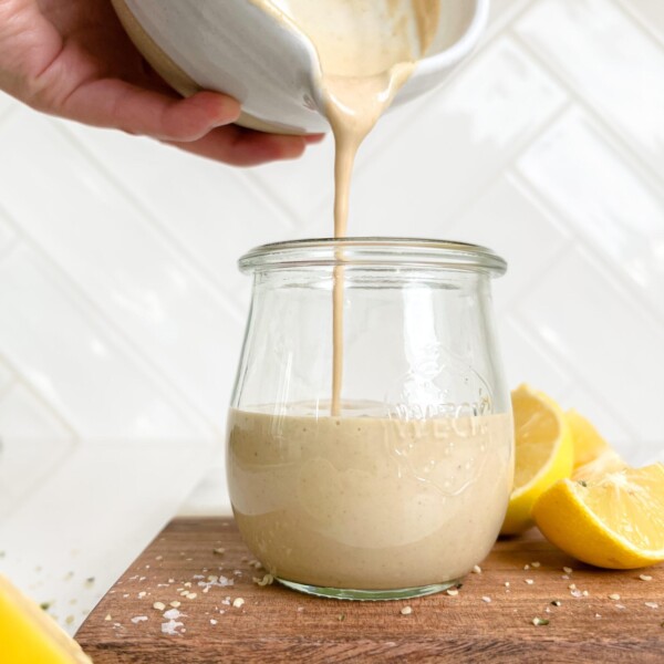 creamy lemon tahini dressing in a jar on a cutting board next to lemon wedges