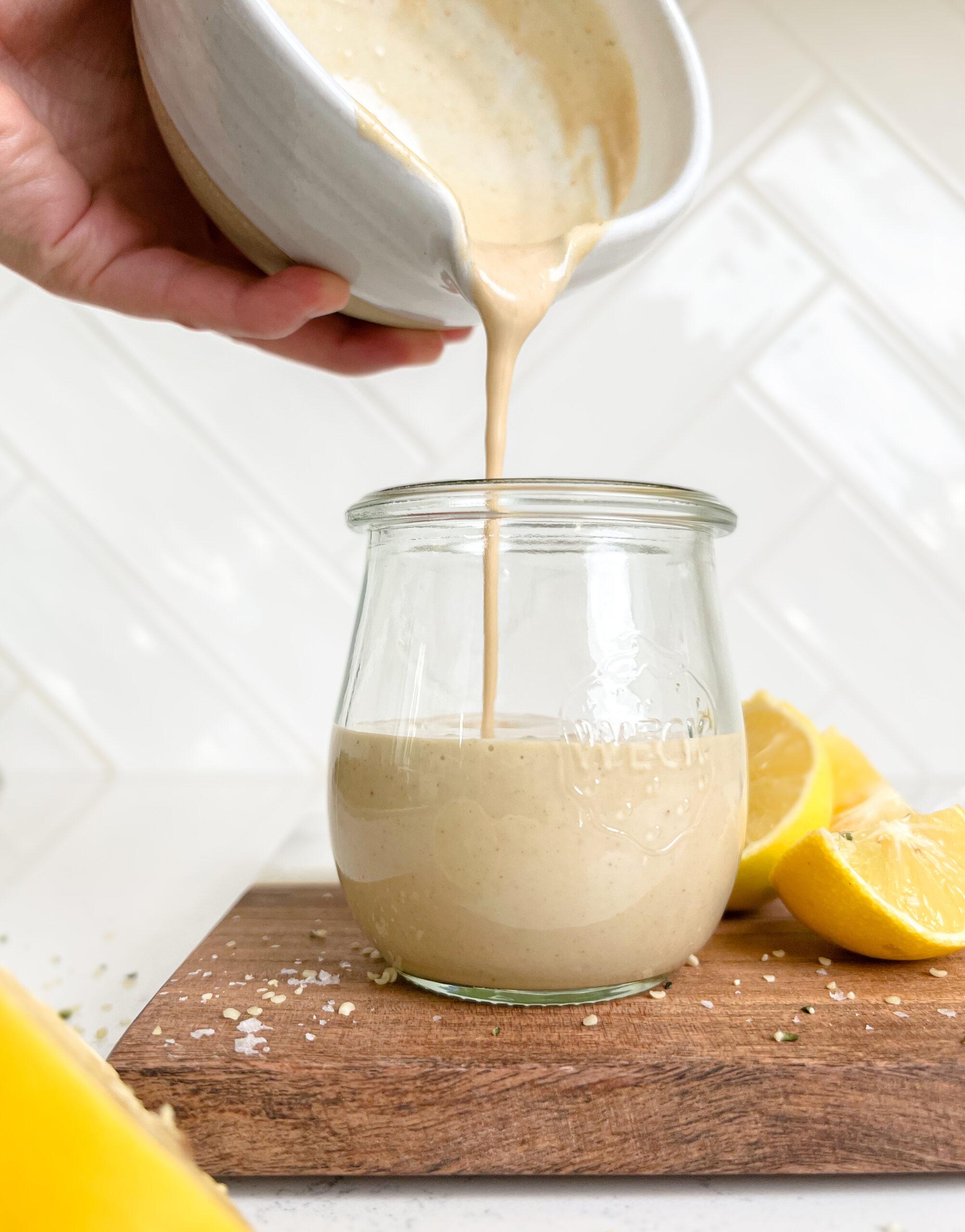 creamy lemon tahini dressing in a jar on a cutting board next to lemon wedges