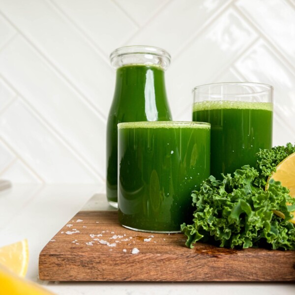 easy green juice in a jar and two glasses on wooden cutting board next to kale and lemons