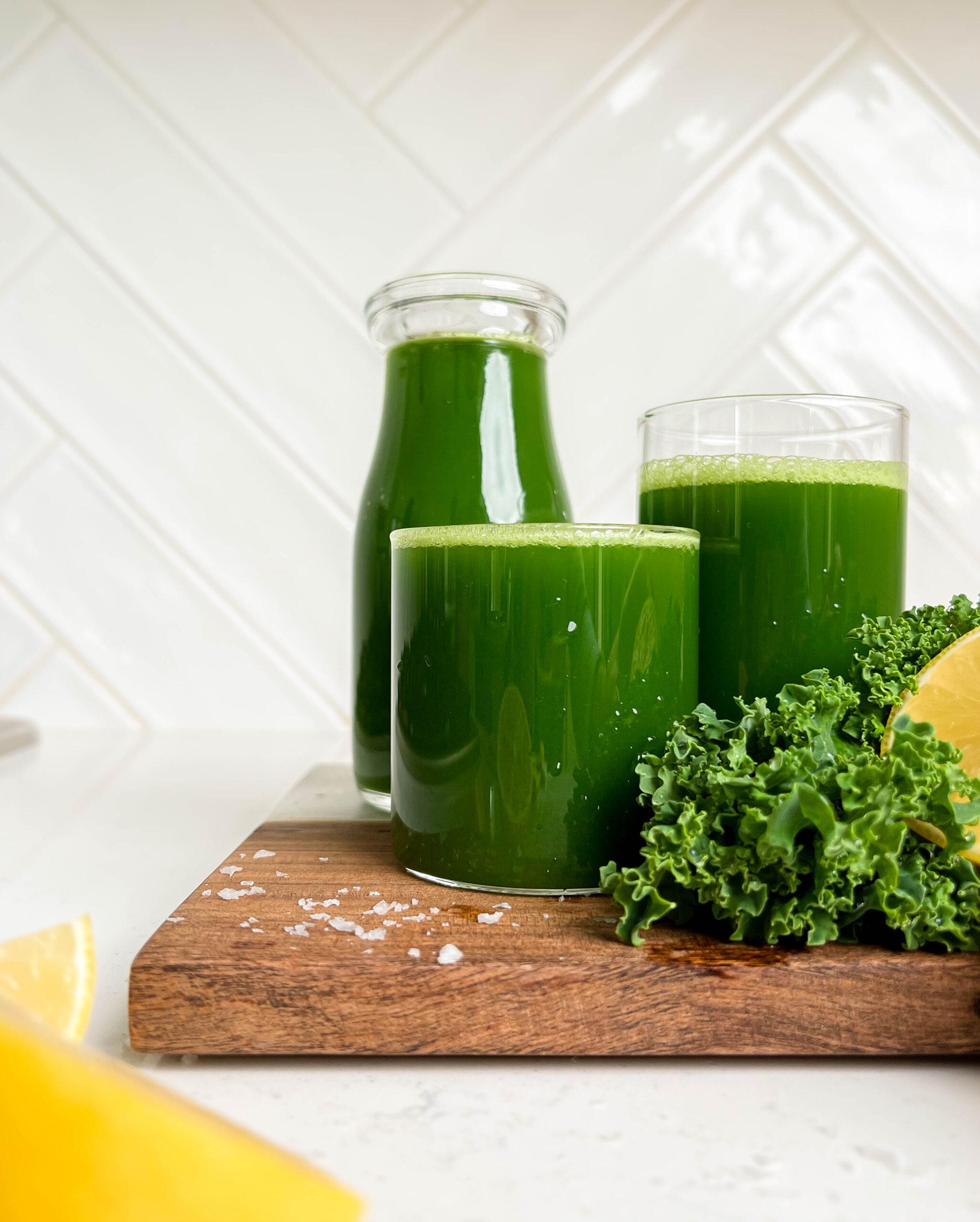 easy green juice in a jar and two glasses on wooden cutting board next to kale and lemons