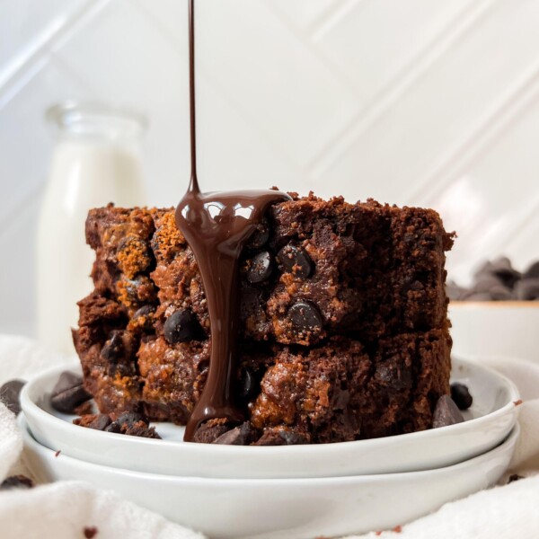 vegan chocolate pumpkin bread slices stacked on a white plate with syrup poured on top